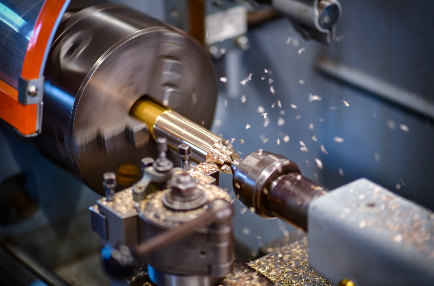 Man sieht eine Drehbank in Aktion, auf der eine Messingstange bearbeitet wird. Metallspäne fliegen durch die Luft – eine Szene aus der Produktion.