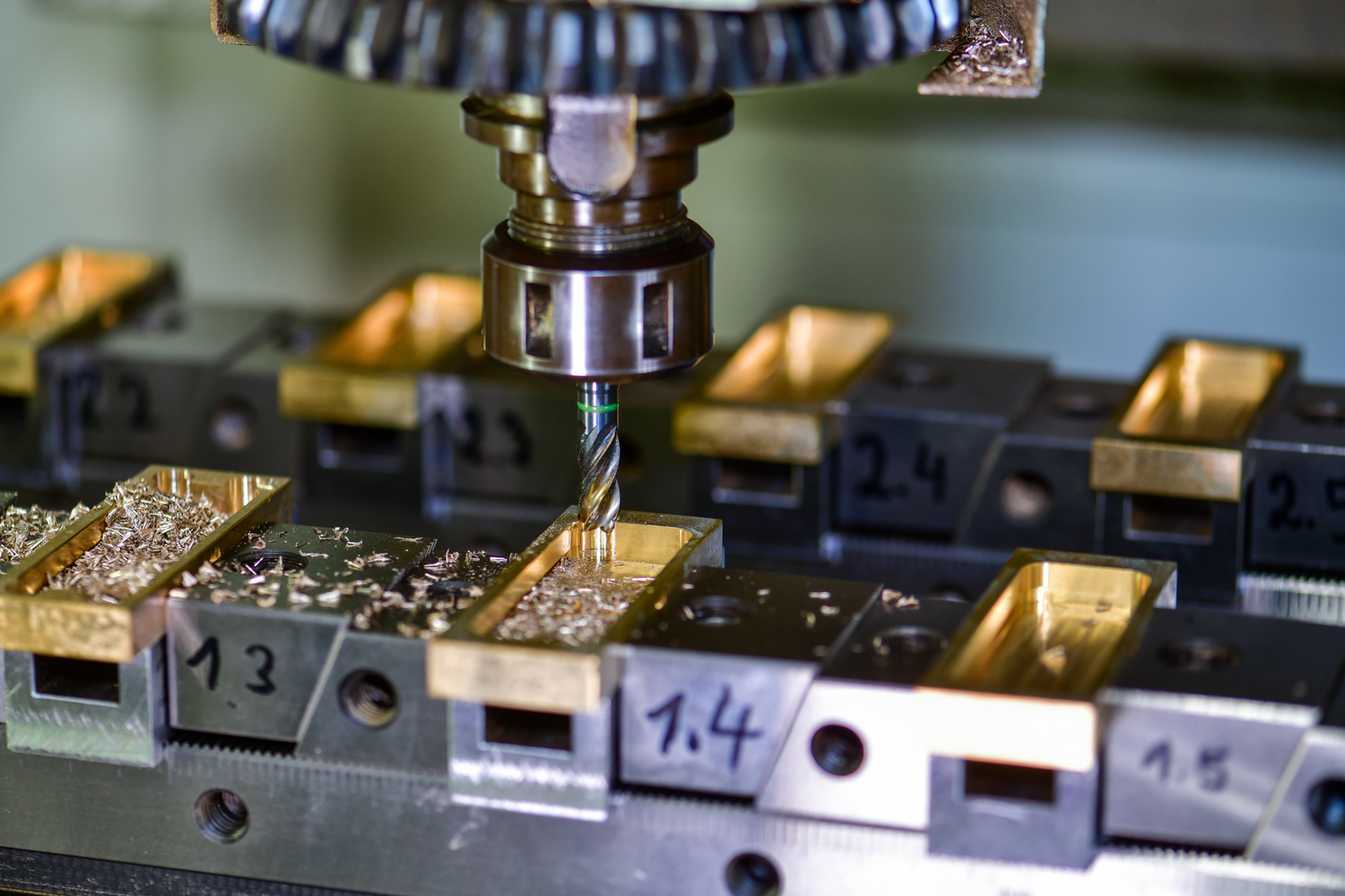 Nahaufnahme einer CNC-Maschine mit rotierendem Fräskopf, der präzise ein rechteckiges Werkstück aus Messing bearbeitet; feine Metallspäne liegen um die Frässtelle.