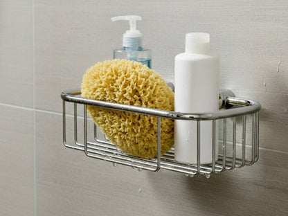 Verchromter Duschkorb zur Wandmontage, gefüllt mit Naturschwamm und Duschgel-Flaschen vor hellgrauen Badezimmerfliesen.